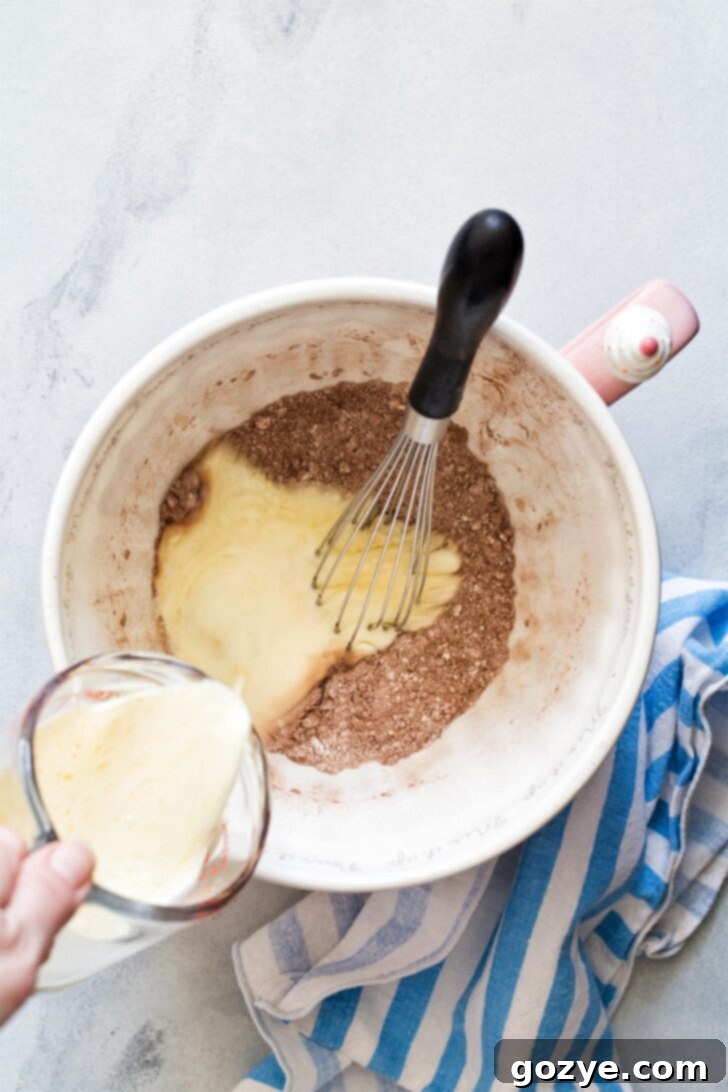 Carefully pouring the mixture of wet ingredients into a bowl containing the dry ingredients, ready for mixing to create chocolate waffle batter.