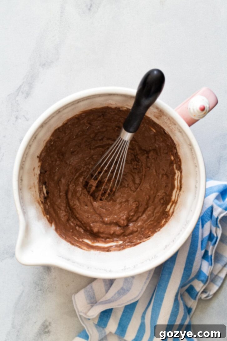 Chocolate waffle batter visibly thickening in a bowl after being left to rest, indicating proper hydration.