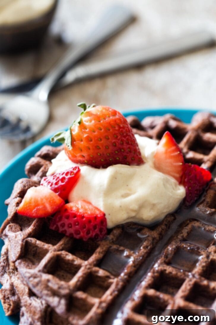 A stack of golden-brown chocolate waffles lavishly topped with homemade peanut butter whipped cream, beautifully presented.