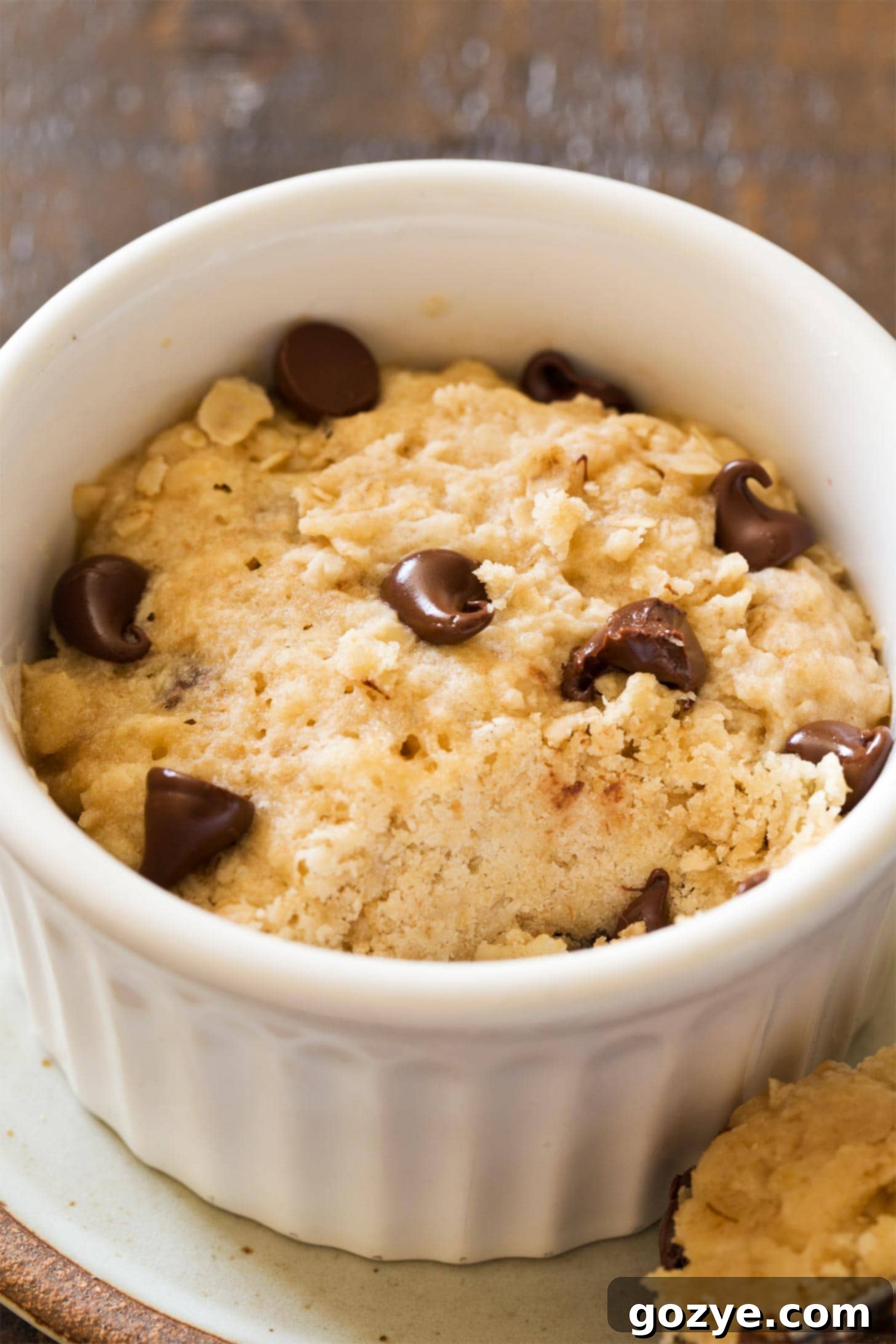 Close-up of a warm microwave oatmeal cookie in a ramekin, showcasing its texture and melted chocolate