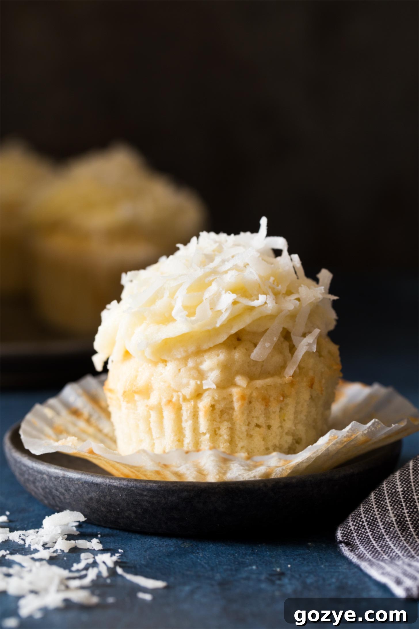 An unwrapped coconut cupcake sitting on a sleek black plate, showcasing its soft, moist crumb and generous frosting.