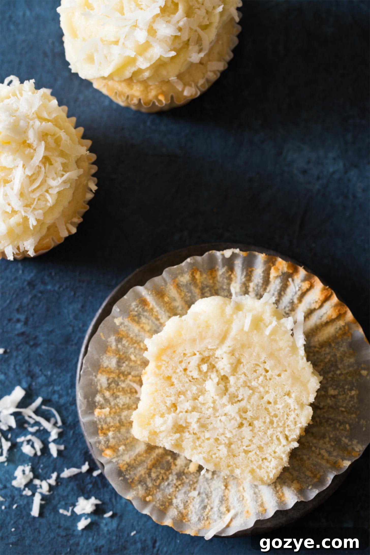 A coconut cupcake sliced in half on a black plate, revealing its moist, tender crumb and the visible shreds of coconut within.