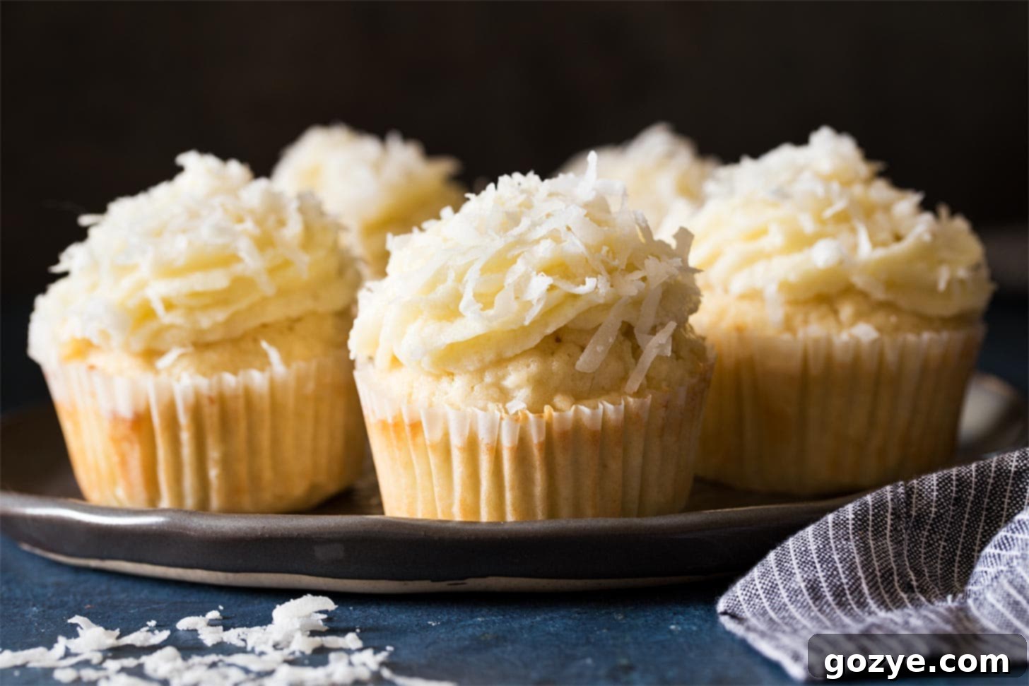 A group of six perfectly baked and frosted coconut cupcakes arranged beautifully on a black plate.