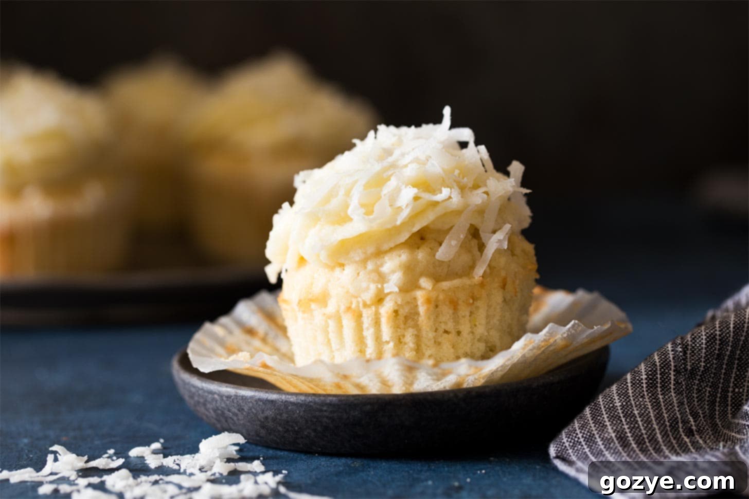 An unwrapped, frosted coconut cupcake on a black plate, ready to be enjoyed.