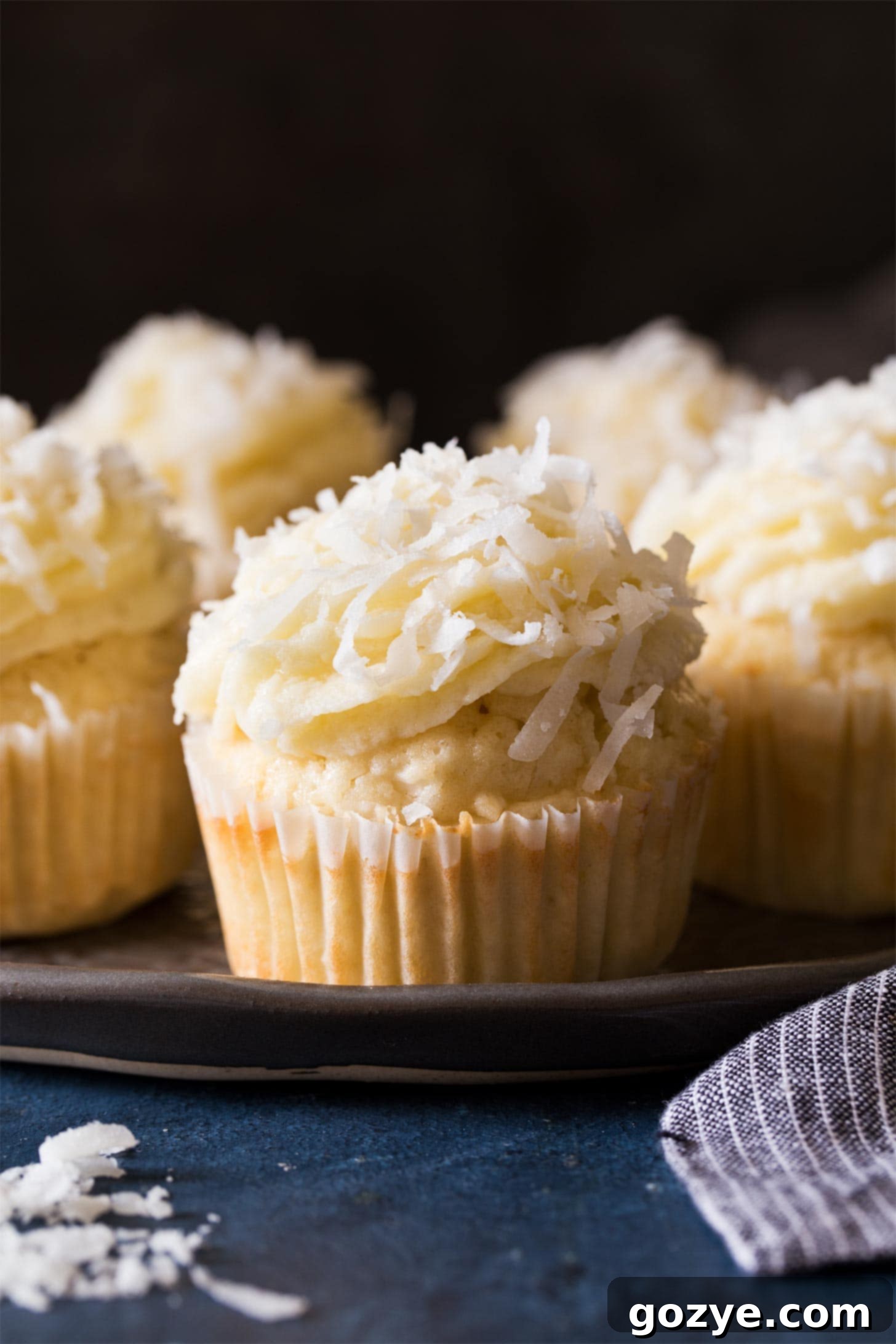 A charming group of coconut cupcakes beautifully arranged on a black plate, ready to be enjoyed.