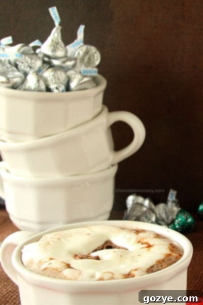Close-up of a Cherry Cordial Kiss sinking into warm hot chocolate topped with whipped cream, illustrating the chocolate's melting process.