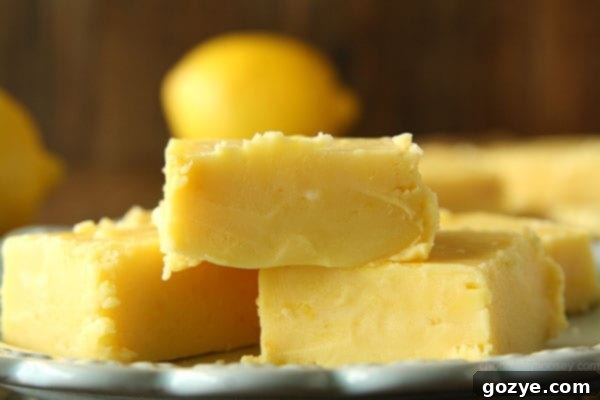 Creamy Lemon Fudge from www.chocolatemoosey.com A close-up of a hand reaching for a piece of creamy lemon fudge, highlighting the soft texture.