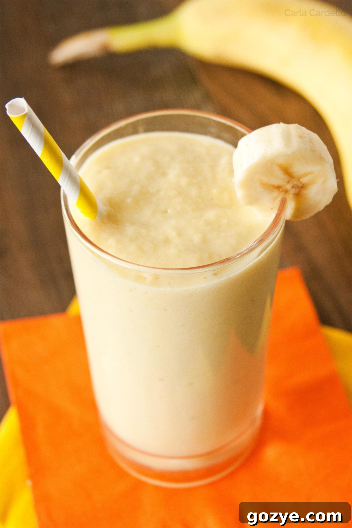 Creamy Banana Mango Smoothie in a glass with a yellow straw, garnished with fresh fruit