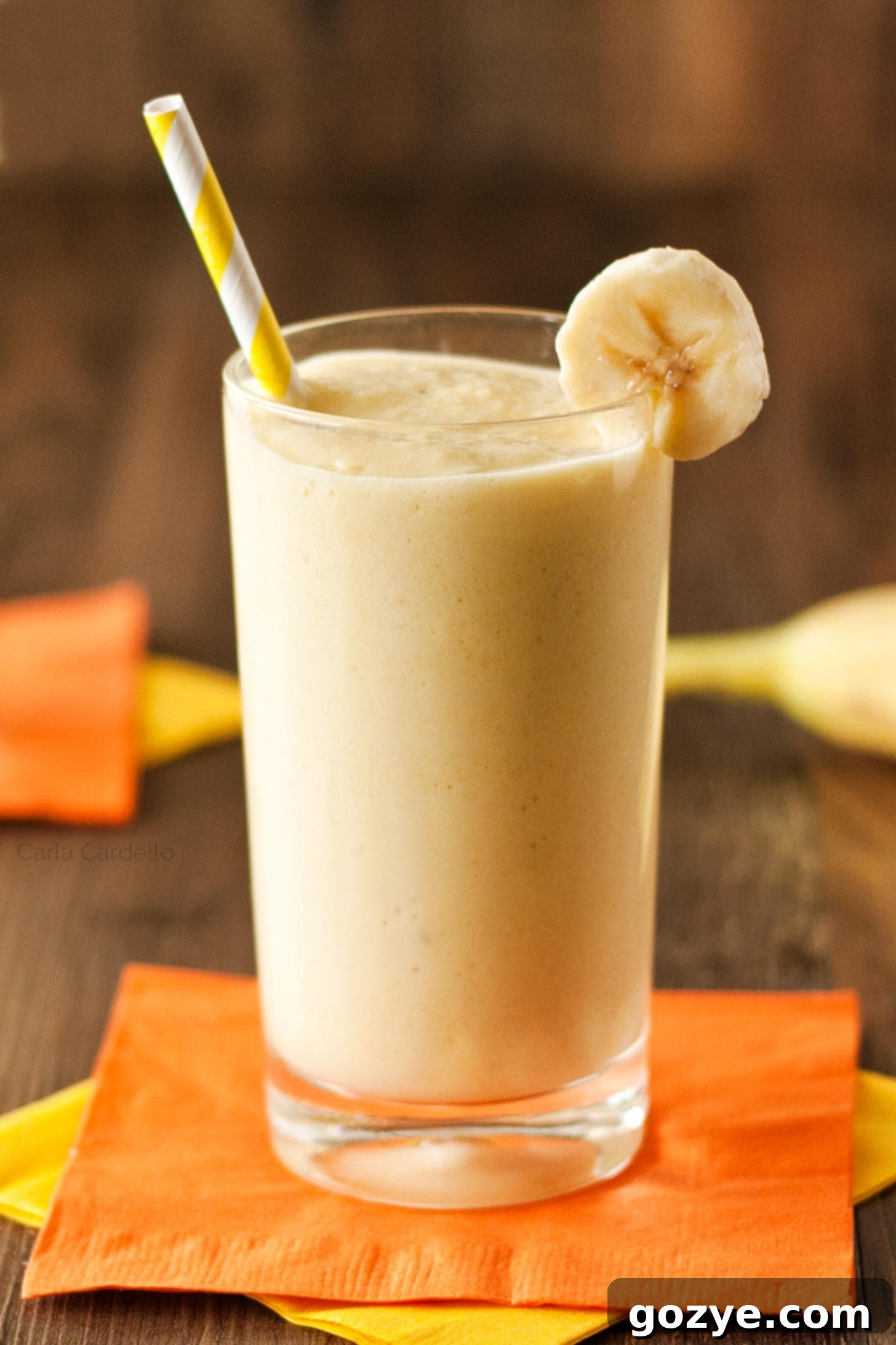 A glass of creamy banana mango smoothie topped with a yellow straw, ready to drink