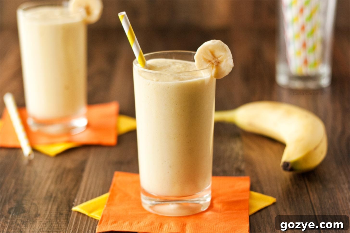 Two vibrant glasses of mango banana smoothie with colorful straws, ready for enjoyment