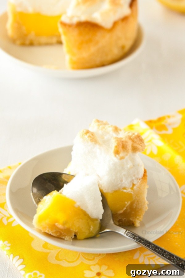 A spoon digging into a mini lemon meringue pie, showing the fluffy meringue and creamy filling.
