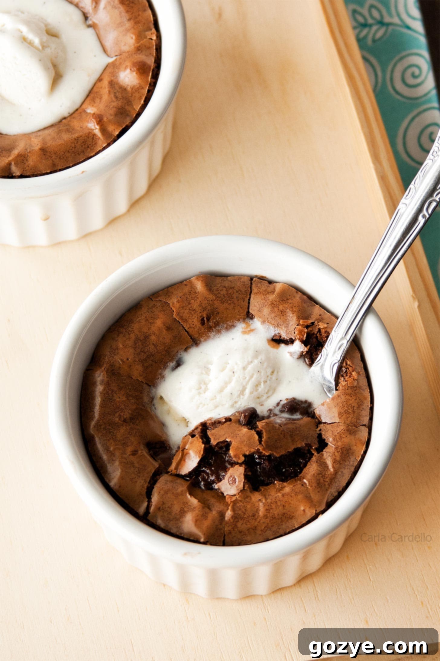 Brownie in a white ramekin with vanilla ice cream on top, ready to be enjoyed.