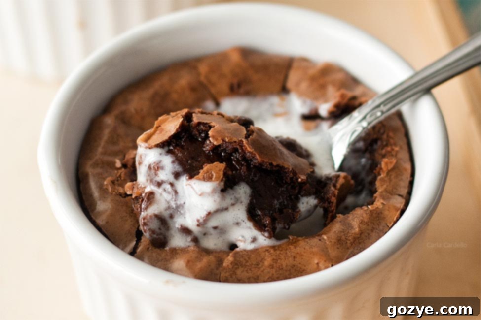 An extreme close-up of a rich, fudgy brownie in a white ramekin, revealing its moist interior and a spoon poised for a bite.