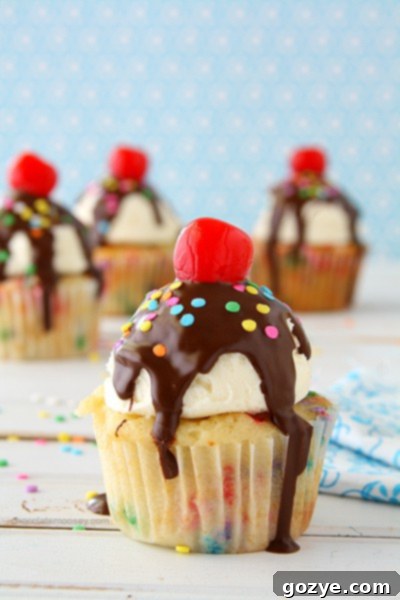 Funfetti Ice Cream Sundae Cupcakes | A close-up view of three Funfetti Ice Cream Sundae Cupcakes on a rustic wooden surface.