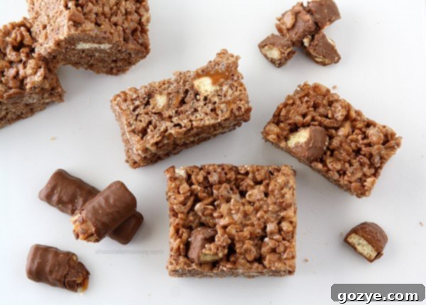 Twix Caramel Chocolate Crispy Bars 3 Close-up of freshly made Chocolate Caramel Twix Rice Crispy Treats, showcasing the melted marshmallow, cereal, and Twix pieces.