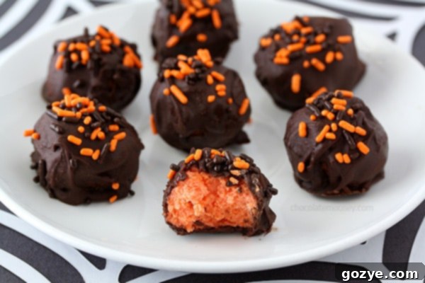 Vibrant orange Halloween Cheesecake Truffles, dipped in dark chocolate and covered with festive sprinkles, arranged on a white serving dish.