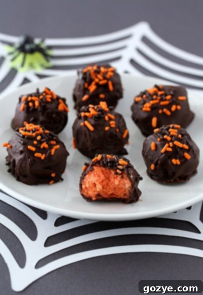 Three Halloween Cheesecake Truffles displayed on a white surface, showing off the vibrant orange cheesecake interior, chocolate shell, and colorful sprinkles.