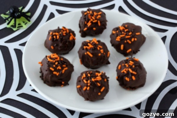 A close-up of a Halloween Cheesecake Truffle, highlighting the smooth chocolate coating and festive orange, black, and white sprinkles.