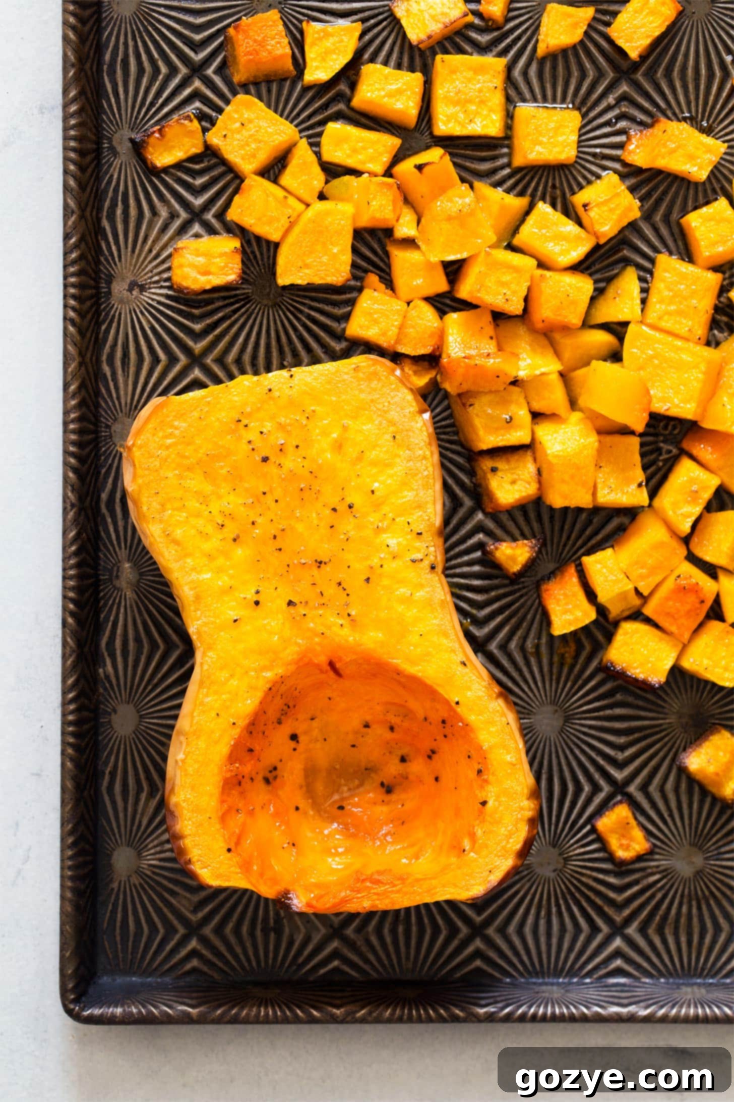 Golden brown roasted butternut squash halves and cubes on a baking tray, ready to be served