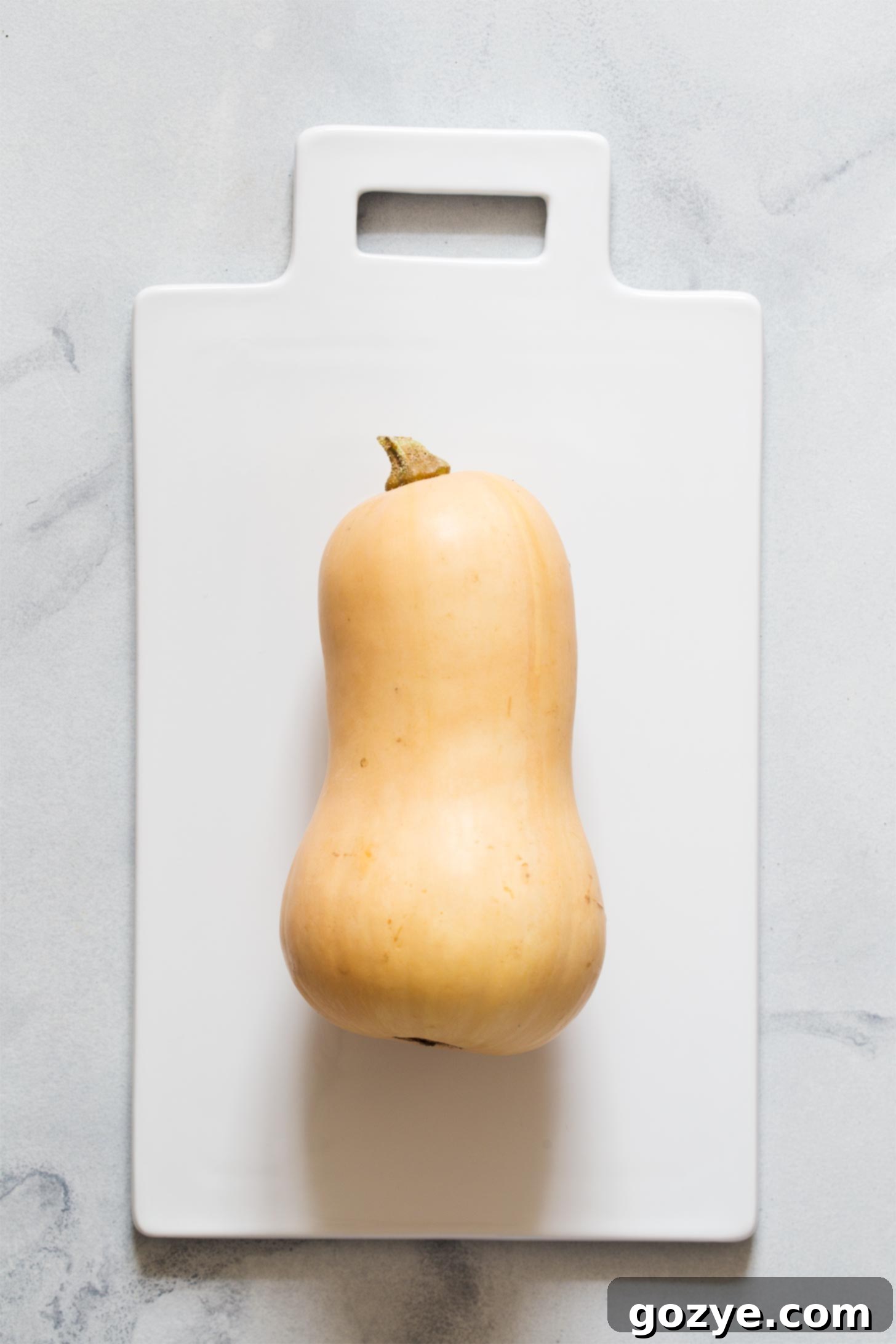 A whole, uncooked butternut squash resting on a wooden cutting board, ready for preparation