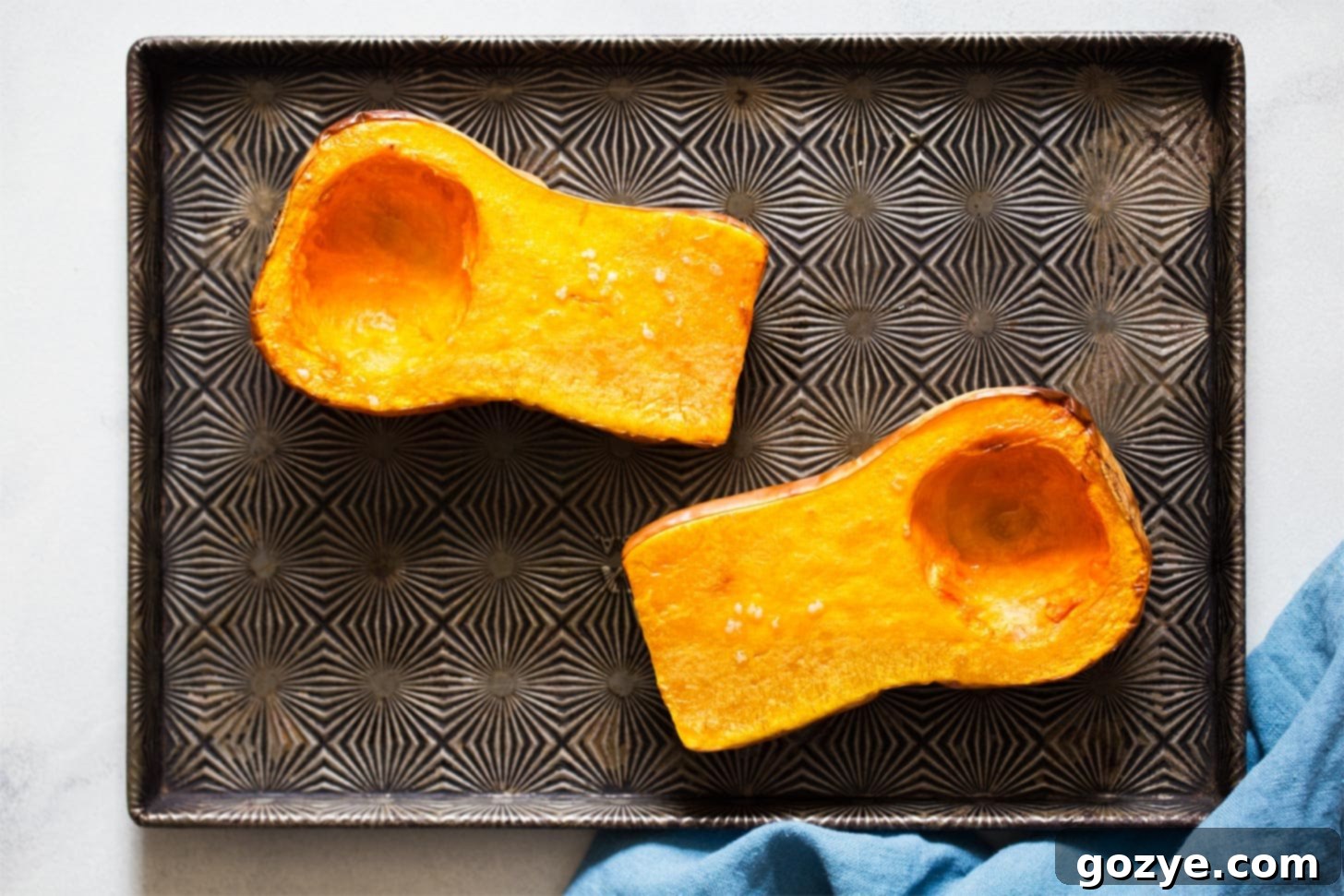 A baking sheet with butternut squash halves being roasted in a hot oven
