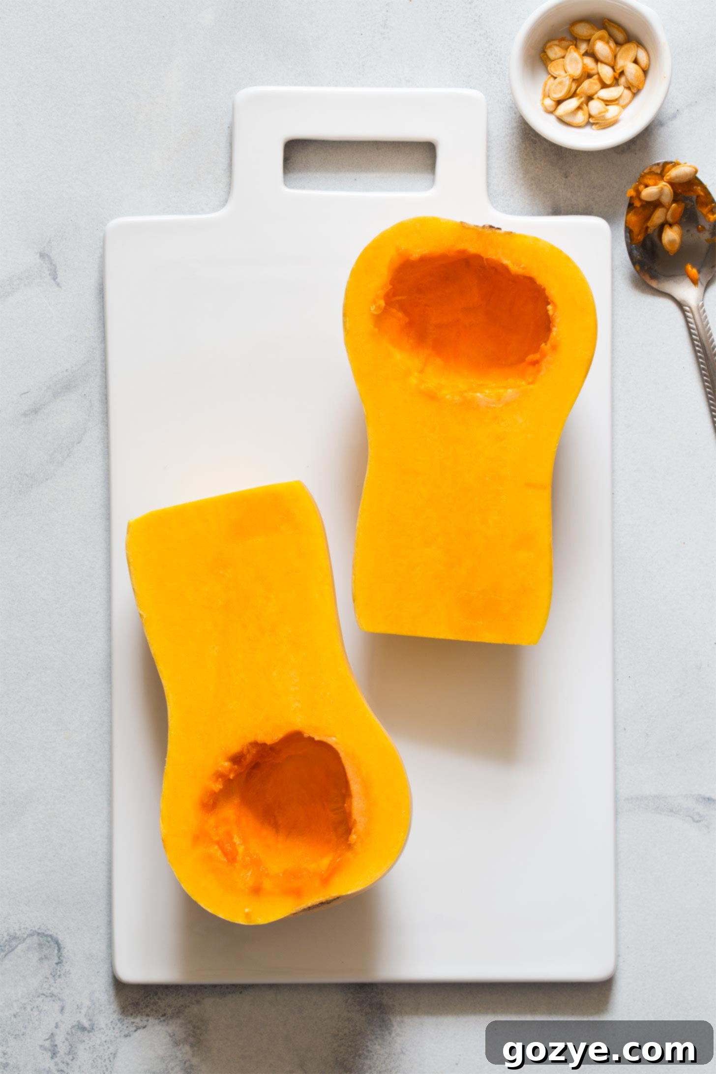 Scooping out the seeds and fibrous strands from the center of a butternut squash half with a spoon