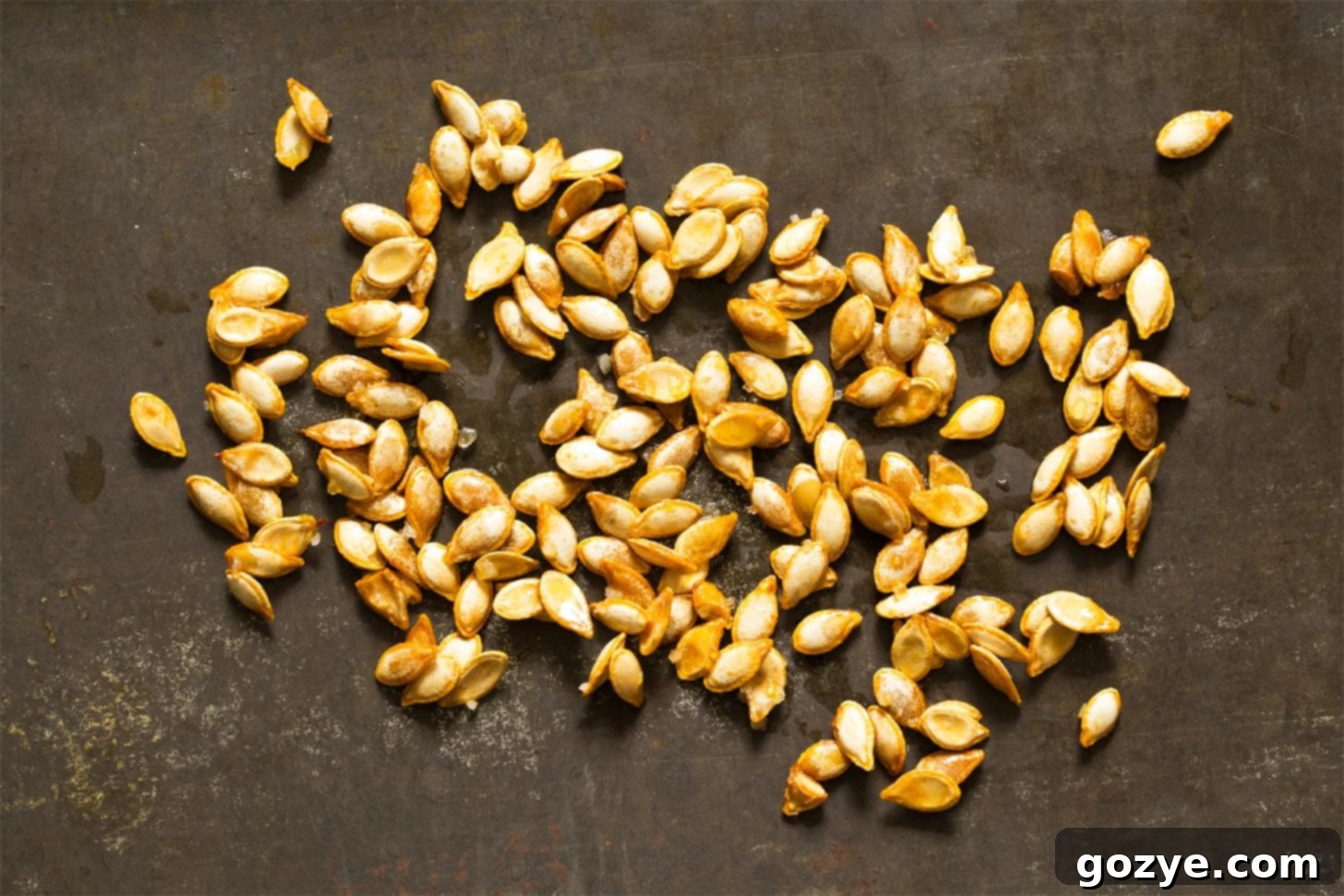 Roasted butternut squash seeds being stirred on a baking tray with a spoon, showing the even distribution during cooking.