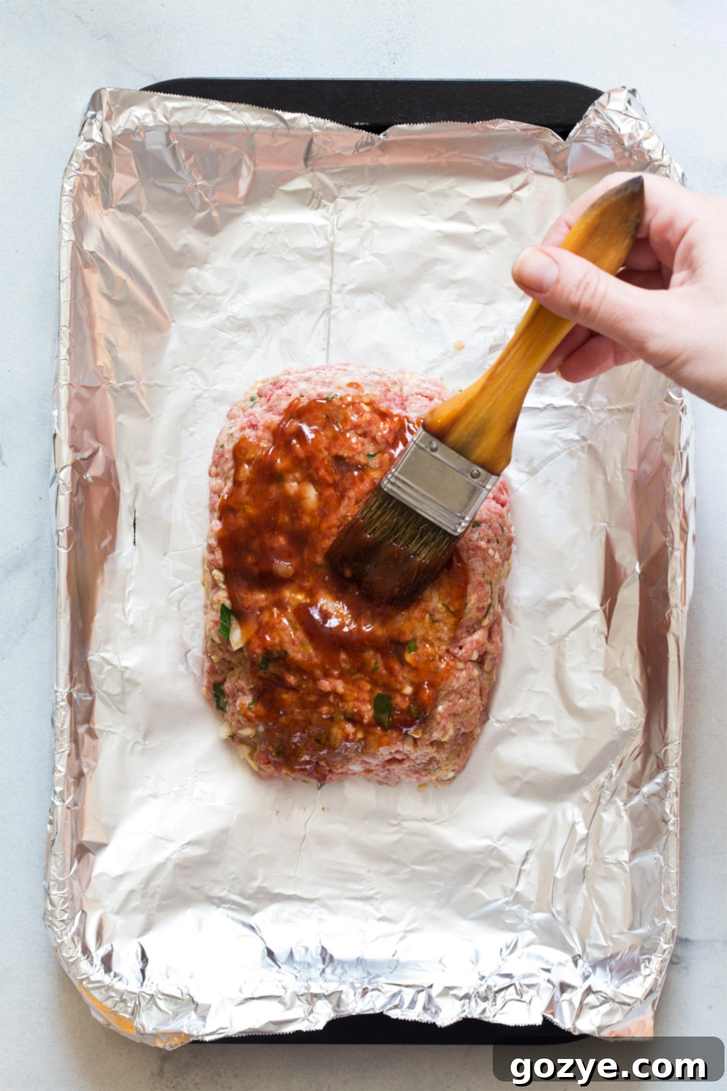 Brushing ketchup glaze on top of mini meatloaf - the final touch for a delicious meatloaf.